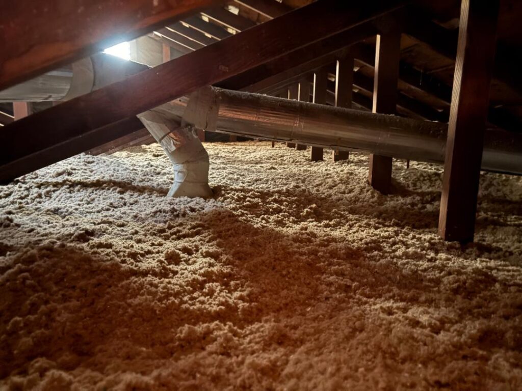 Cellulose insulation filling an attic space under wooden rafters.