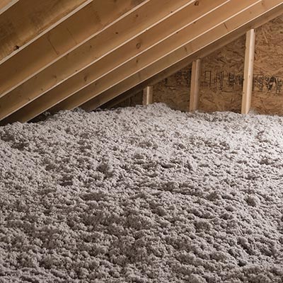 Loose-fill cellulose insulation filling an attic space under wooden rafters.