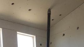 Drywall installation with a pipe extending from the ceiling.