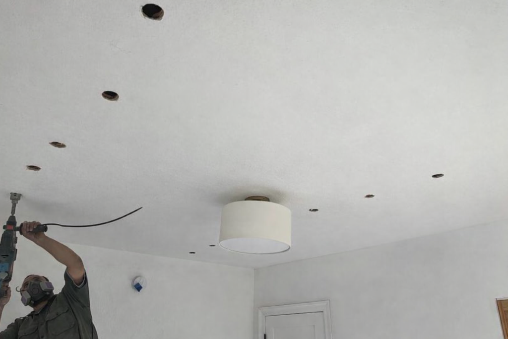 Man drills holes in ceiling for home lighting installation
