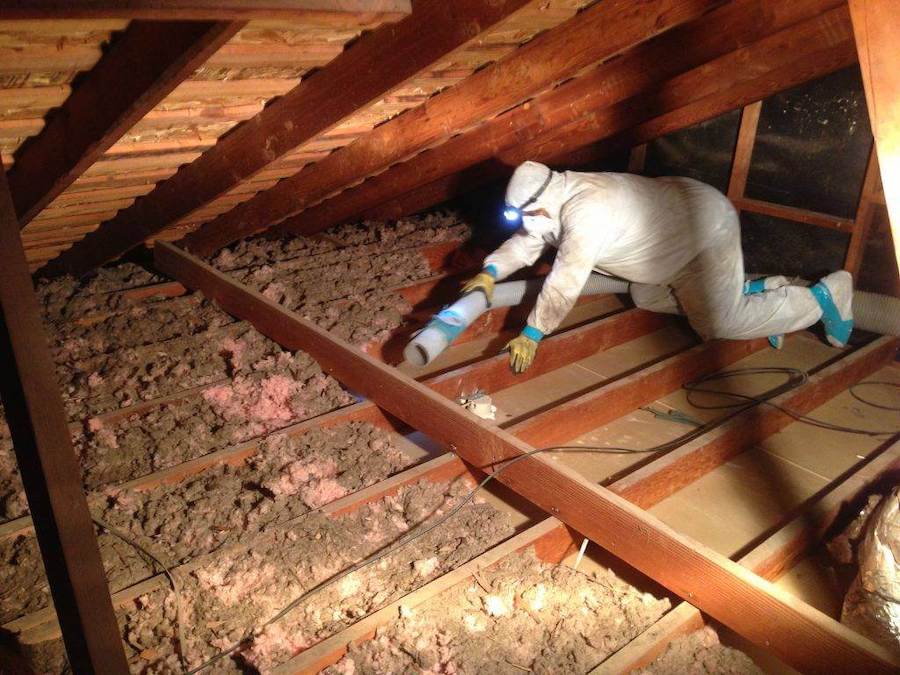 Worker in protective suit installing fiberglass insulation in attic
