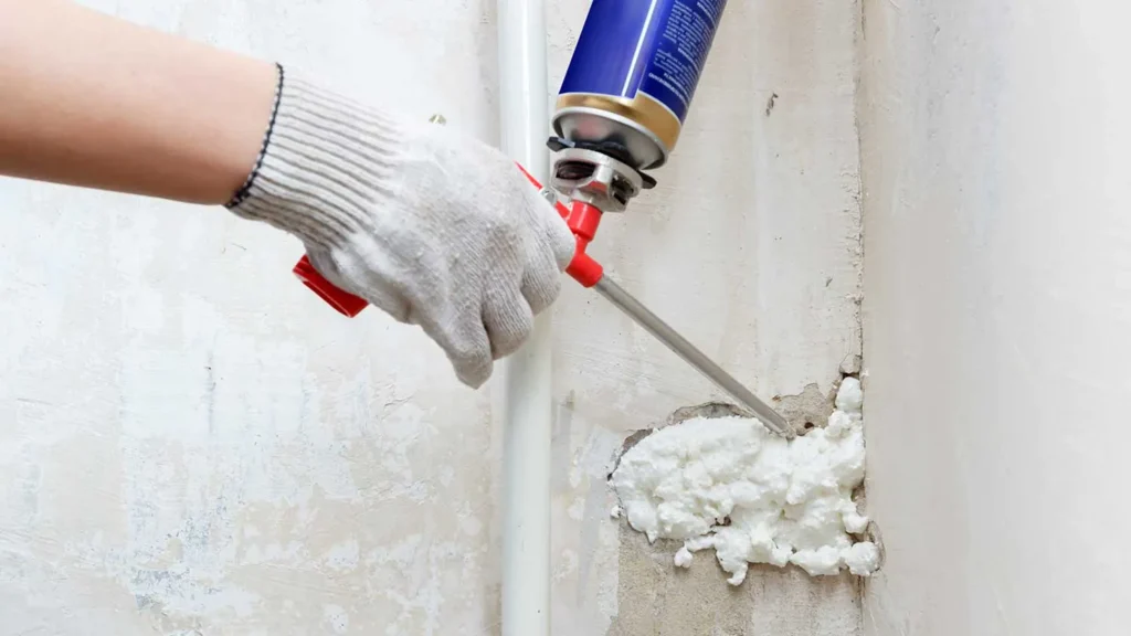 Hand in glove applying expanding foam to fill a wall crack