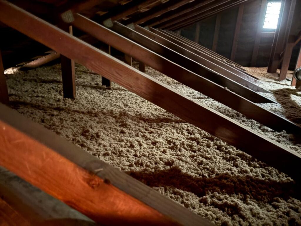 Cellulose insulation filling an attic space beneath wooden rafters.