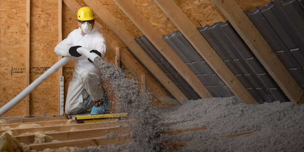 Man in protective gear blowing cellulose insulation in attic